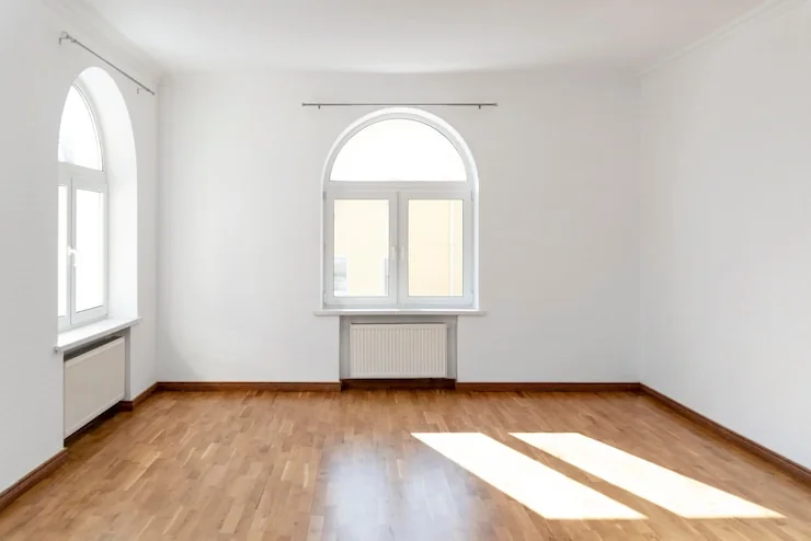 An empty white room after rubbish removal, sun on the wooden floor and a radiator under the window