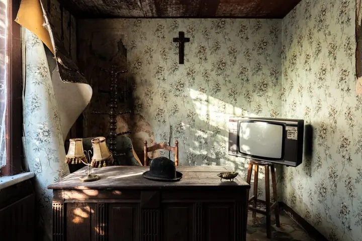 An old room with floral wallpaper, a wooden desk and an old television on legs