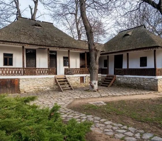 An old white village house with a porch and a clear yard with a stone path