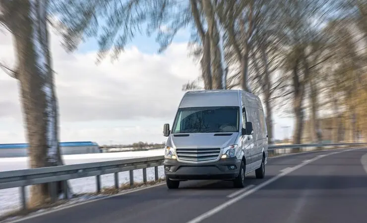 A white Mercedes Sprinter van on a country road in winter