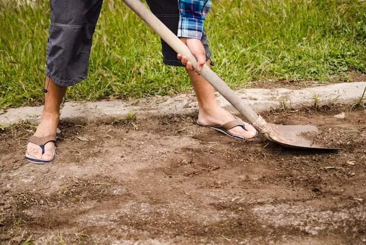 Someone in flip-flops digging up soil in a yard with a shovel