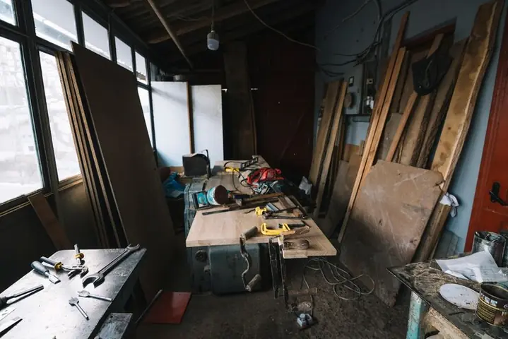 An old workshop with planks against the wall, tools and a cluttered workbench