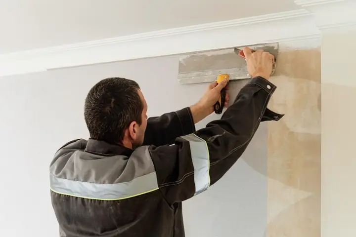 A worker scraping old wallpaper off a wall in a flat under renovation